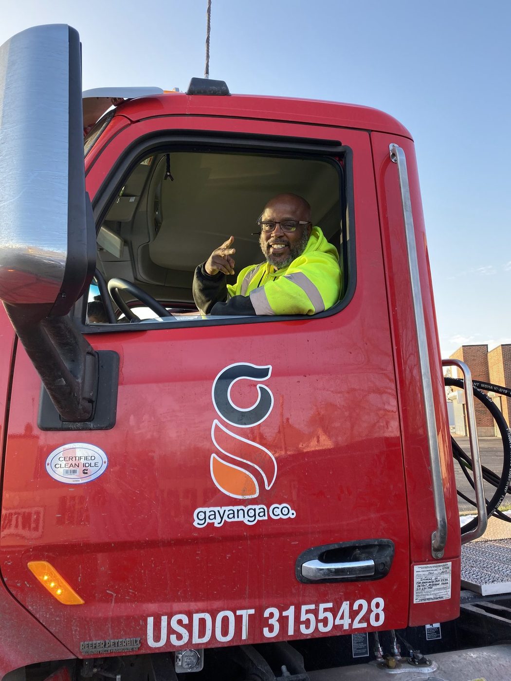 A Gayanga Co. driver smiling from the cab of a company Peterbilt