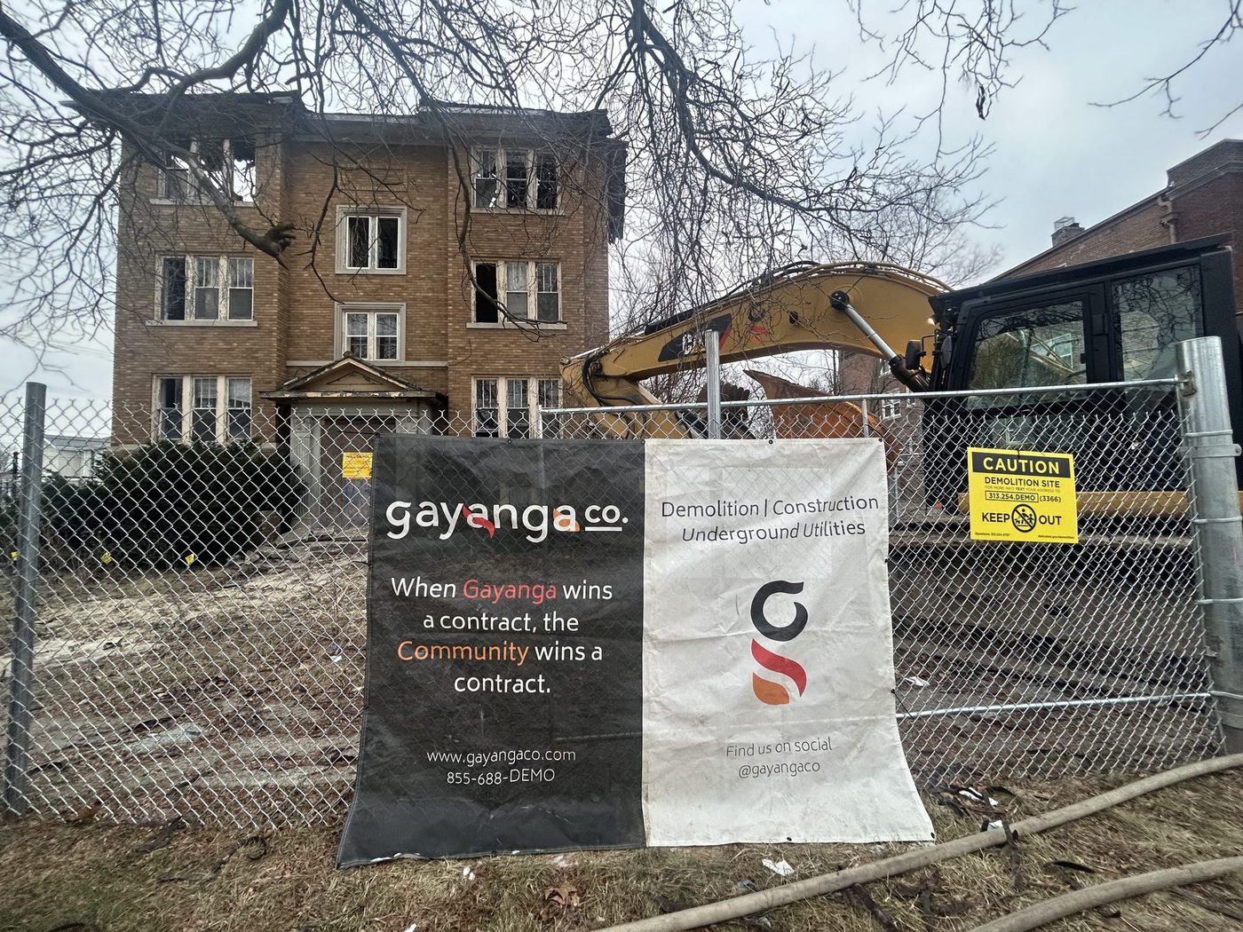 Gayanga banner on the fence of an apartment demolition site with a CAT excavator