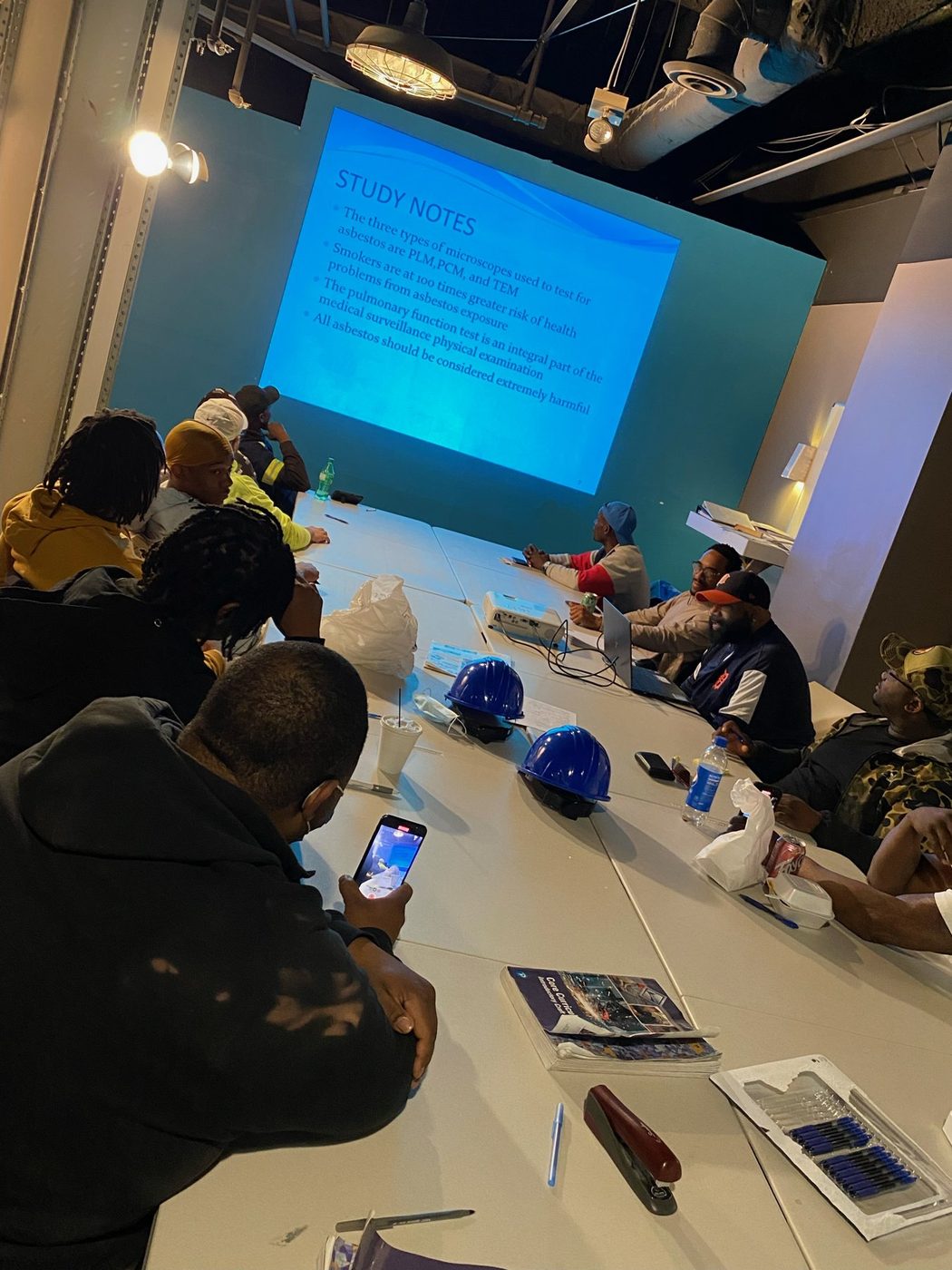 Gayanga workforce trainees in an asbestos-abatement classroom session, hard hats on the table