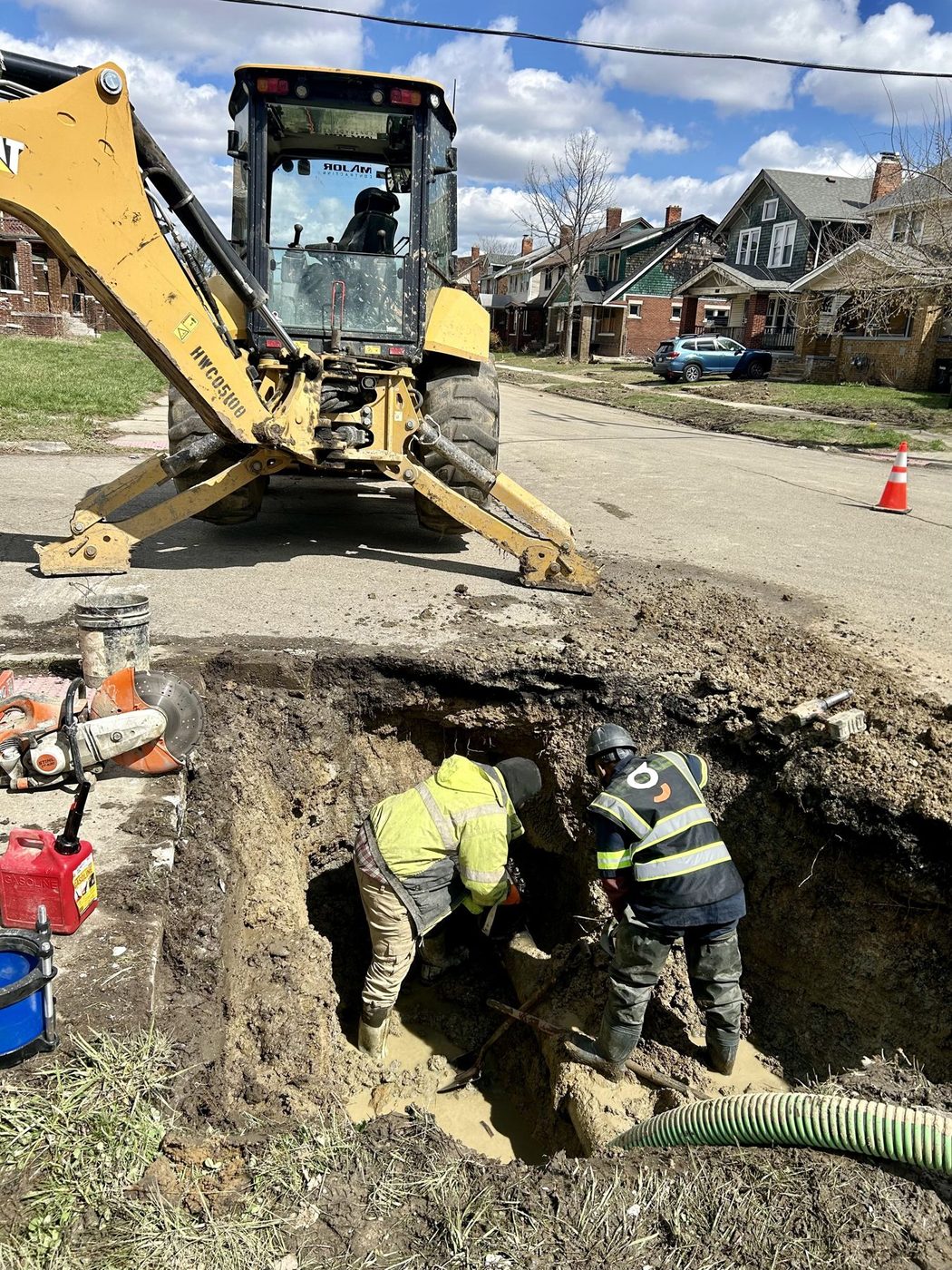 Gayanga crew and backhoe in a water main trench on a Detroit residential street, 2025