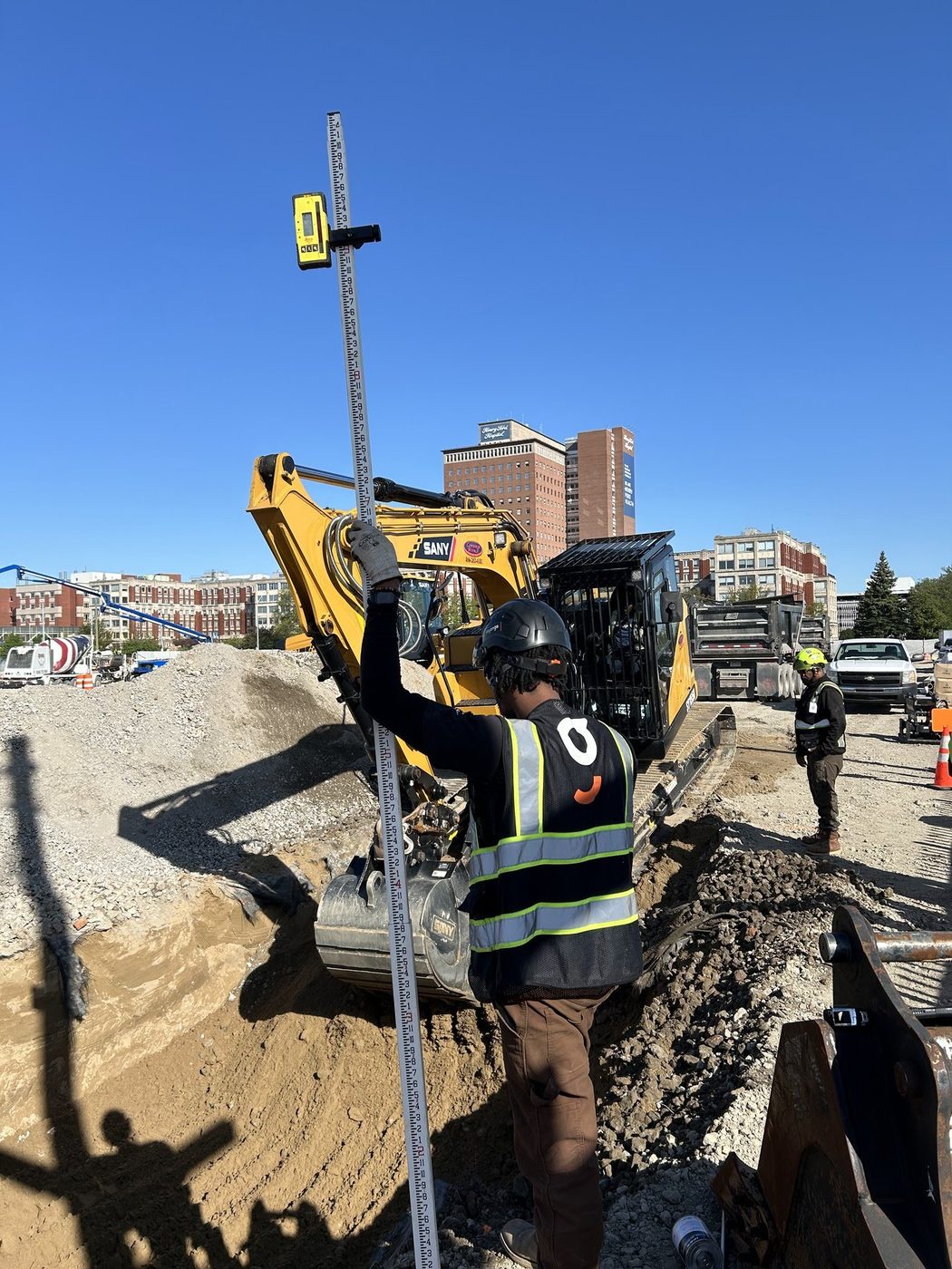 A Gayanga laborer checking grade with a laser level in a water main trench, 2025